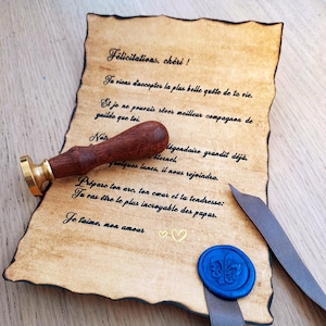Peut inclure: Un parchemin de style vintage avec un texte manuscrit, un tampon de cire en bois et or, un sceau de cire bleu et un ruban gris. Le parchemin a un aspect vieilli avec des bordures noires et des détails de cœur dorés.