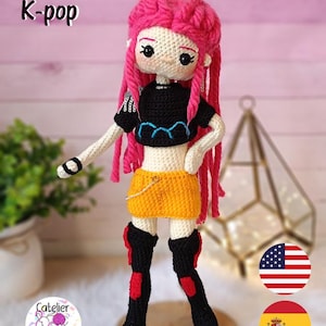May include: Crocheted doll with pink hair and a black top, yellow skirt, and black boots with red accents. The doll is labeled "Huntrix girl K-pop". The doll is standing on a wooden base.