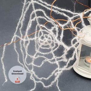 Pode incluir: Uma teia de aranha branca, feita à mão com fio, é drapeada sobre galhos, ao lado de uma lanterna branca com uma vela acesa dentro. A lanterna tem recortes de estrelas. As palavras "Download instantâneo" estão na imagem.