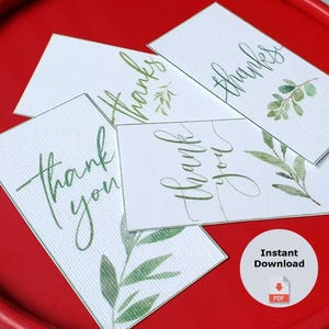 Puede incluir: Etiquetas de regalo blancas con escritura verde que dice "gracias" y "gracias", con acentos de hojas de acuarela. Las etiquetas est&aacute;n dispuestas en una bandeja roja. La imagen tambi&eacute;n incluye un icono de etiqueta de regalo imprimible de bonificaci&oacute;n.