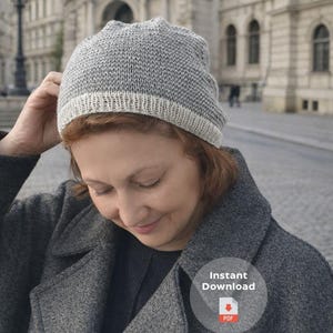 Puede incluir: Un gorro de punto gris con un borde color crema. El sombrero lo lleva una persona que lleva un abrigo gris. El fondo es una calle y edificios de la ciudad borrosos. La imagen también contiene el texto "Descarga instantánea" y un icono PDF.