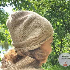 Pode incluir: Um gorro de malha bege com uma aba dobrada. O chapéu é feito de um fio macio e texturizado. O fundo mostra um cenário natural verde com árvores e água. A imagem inclui um pequeno gráfico circular com as palavras "Download instantâneo" e um ícone PDF.