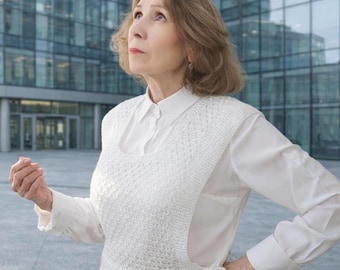 May include: A white long-sleeved button-down shirt layered under a white sleeveless knit vest. The vest features a textured, open-weave pattern across the front and a single visible button closure at the lower side, creating a layered ensemble.