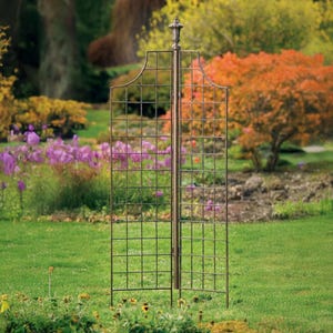 May include: A metal garden trellis with a decorative finial on top. The trellis is made of a square grid pattern and is freestanding. It is shown in a garden setting with green grass and flowers.
