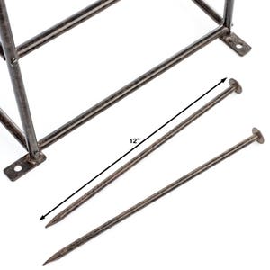 May include: A dark brown metal frame with two matching metal stakes. The stakes are pointed at one end and have a flat circular head at the other. A dimension line indicates the stakes are 12 inches in length. The frame has mounting tabs.