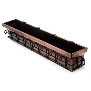 May include: A copper window box planter with a black metal scrolled design. The planter is rectangular and has a slightly curved front edge.