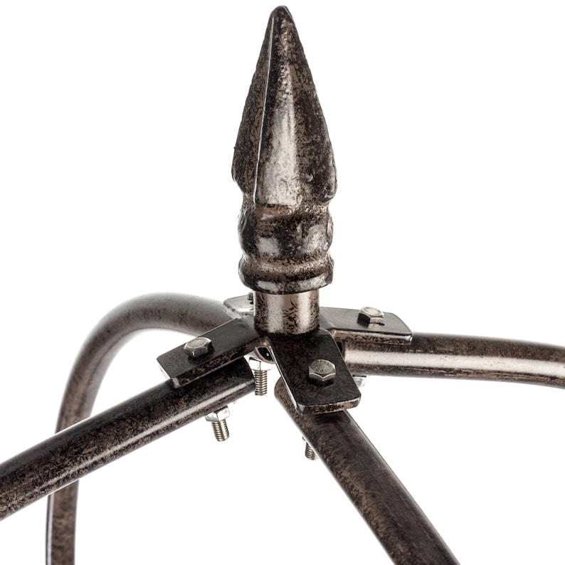 May include: A dark bronze-colored metal finial with a pointed spear-like top, attached to a curved metal frame structure. The assembly is secured with small silver-colored metal bolts and nuts at the central junction point of the frame.