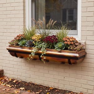 May include: A rectangular copper window box planter with a dark metal frame, filled with a variety of autumn plants including yellow, orange, and deep red chrysanthemums, green ornamental kale, trailing ivy, and tall ornamental grasses.