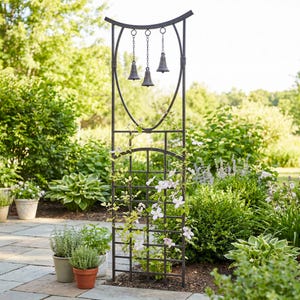 May include: A dark metal garden trellis with a curved top and three hanging bells. The trellis has a grid pattern and is adorned with climbing plants with white flowers. The scene is set outdoors with lush greenery.