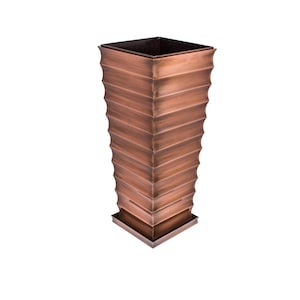 May include: A copper-colored metal planter with a square shape and a textured, layered design. The planter has a wide base and a narrow top.
