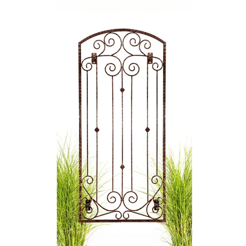 Pu&ograve; includere: Un alto traliccio da parete rettangolare in metallo con finitura marrone scuro e texture martellata. Il design presenta una parte superiore ad arco, barre verticali con piccole sfere decorative e complessi motivi a volute in alto e in basso.