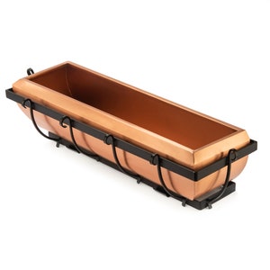 May include: A copper-colored planter with a black metal frame. The planter is rectangular and has a curved bottom. The frame has decorative scrolls on the sides.