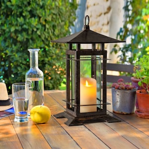 May include: A black metal lantern with a glass panel and a white candle inside. The lantern is sitting on a wooden table with a glass of water and a lemon beside it.