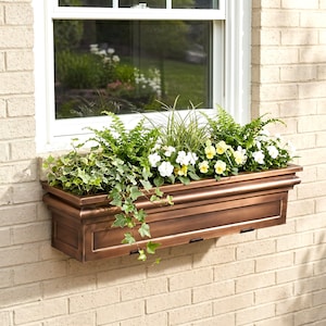 May include: A rectangular copper-toned window box planter mounted on a light-colored brick wall. The planter is filled with a variety of green foliage, including trailing ivy, upright ferns, and small white and yellow pansy flowers.