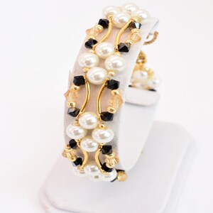May include: A gold bracelet with black and white beads. The bracelet is made of pearls, crystals, and gold wire.