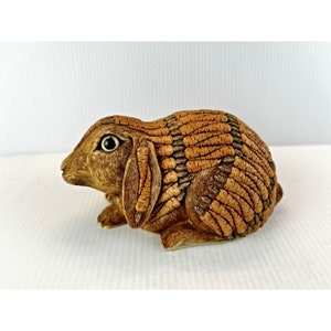 May include: A brown ceramic rabbit figurine with a textured, segmented body. The rabbit has a small, black eye and a long, floppy ear.