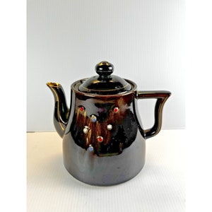 May include: A brown ceramic teapot with a gold trim and colorful accents. The teapot has a lid and a spout.