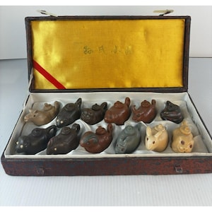 May include: A set of twelve miniature animal-shaped teapots in a decorative box. The teapots are various shades of brown, gray, and beige. The box has a gold interior and a red ribbon. The box is brown with a decorative pattern.