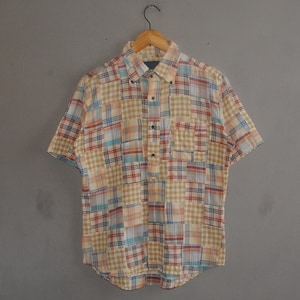 May include: A short-sleeved button-down shirt with a patchwork plaid pattern in shades of blue, red, yellow, and brown.