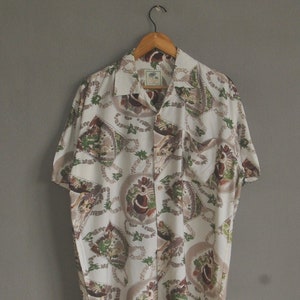 May include: A white short-sleeved button-down shirt with a colorful floral pattern. The shirt has a collar and a pocket on the left side.
