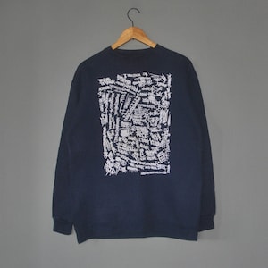 May include: A navy blue sweatshirt with a white graphic print of a large square filled with handwritten text.