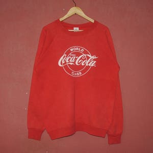May include: Red Coca-Cola sweatshirt with a white logo that says "World Enjoy Coca-Cola Class".