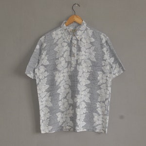 May include: A gray and white short-sleeved button-down shirt with a floral print. The shirt has a collar and a button-up front.