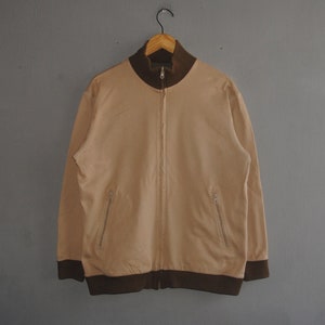 May include: A beige zip-up jacket with brown ribbed trim around the collar, cuffs, and hem. The jacket has two zippered pockets on the front.