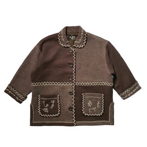 Peut inclure: Une veste en laine mélangée marron avec un panneau en tissu marron contrastant et des détails brodés. La veste a une fermeture boutonnée à l'avant et un col avec une bordure cousue.
