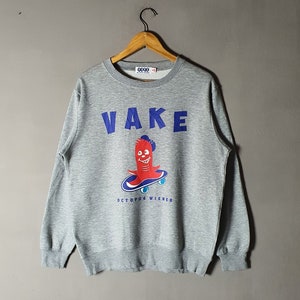 May include: Grey sweatshirt with a blue and red graphic of a cartoon octopus riding a skateboard. The text "VAKE" is printed in blue above the octopus and "OCTOPUS WIENER" is printed in blue below the octopus.