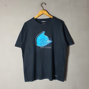 May include: Black t-shirt featuring a blue and white graphic of Astro Boy. The graphic includes the text "Astro Boy", "In 2003 a robot", "created by Dr. Tenma", "mobilizing the core", "of technologists", "The robot was named", "Astro Boy", "APR.7.2003".