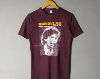 May include: A maroon t-shirt with a white image of Bob Dylan and the text "Bob Dylan European Concert Tour 1981" in yellow.