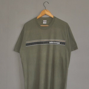 Puede incluir: Una camiseta verde con una banda negra, blanca y marrón a través del pecho. La banda tiene la palabra "bluetones" impresa en letras blancas.