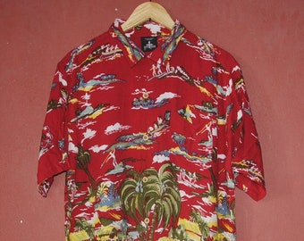 May include: A red short-sleeved button-down shirt with a tropical print featuring palm trees, huts, and people. The shirt has a white collar and a button-up front.