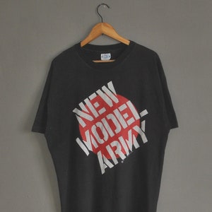 Könnte beinhalten: Schwarzes T-Shirt mit einem roten Kreis und weißem Text, der "NEW MODEL ARMY" lautet.