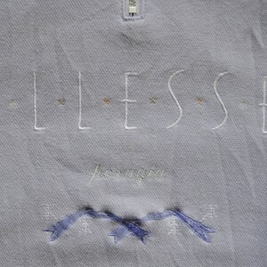 May include: A light blue sweatshirt with the word "ELLESSE" embroidered in white with small colored accents. The word "Aeronautica" is embroidered in white below the logo. The sweatshirt has a zipper at the top.