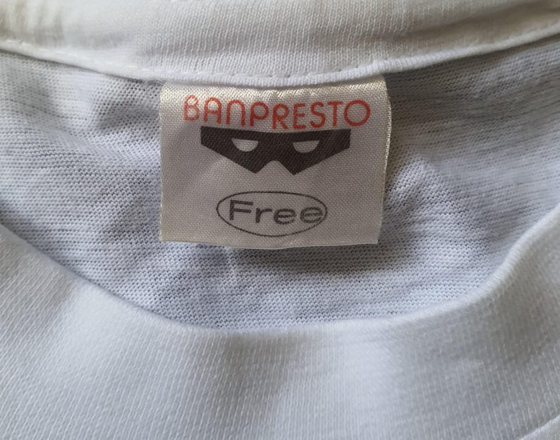 May include: White t-shirt with a Banpresto label featuring a black mask logo and the word "Free" in a circle.