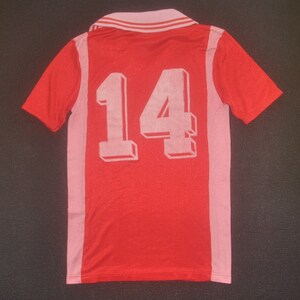 Op de afbeelding: Rood voetbal shirt met roze accenten en het nummer 14 gedrukt op de rug.