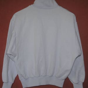 May include: A light blue, long-sleeved sweatshirt with a mock neck and a ribbed hem.