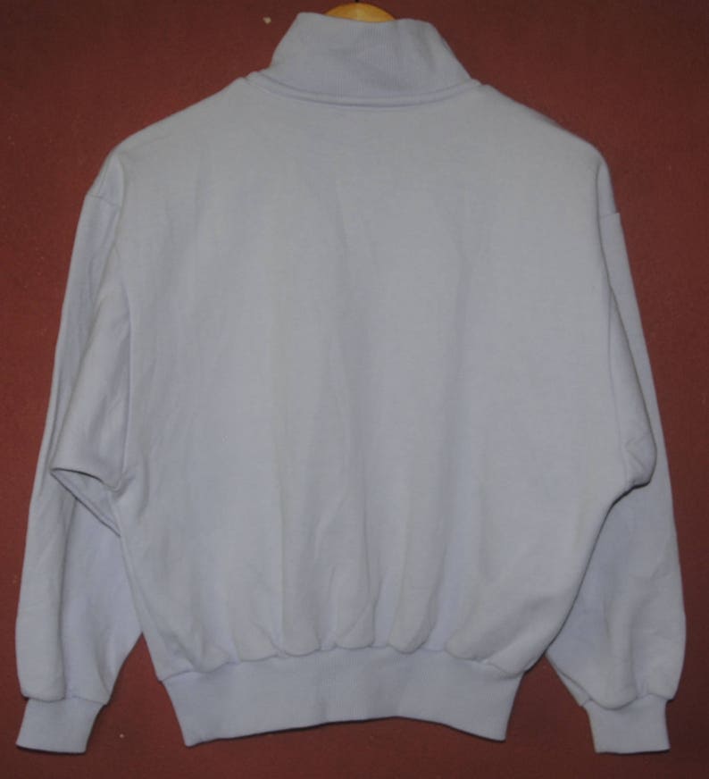 May include: A light blue, long-sleeved sweatshirt with a mock neck and a ribbed hem.