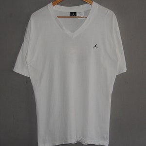 K&ouml;nnte beinhalten: Wei&szlig;es T-Shirt mit V-Ausschnitt und kleinem schwarzem Jumpman-Logo auf der Vorderseite.