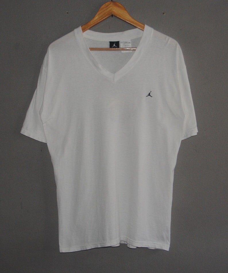 K&ouml;nnte beinhalten: Wei&szlig;es T-Shirt mit V-Ausschnitt und kleinem schwarzem Jumpman-Logo auf der Vorderseite.
