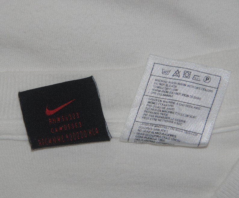 K&ouml;nnte beinhalten: Ein wei&szlig;es T-Shirt mit einem schwarzen Pflegeetikett und einem schwarzen Etikett mit dem Text "RN# 56323 CA# 05553  NIKE HWY 920220 KLA"