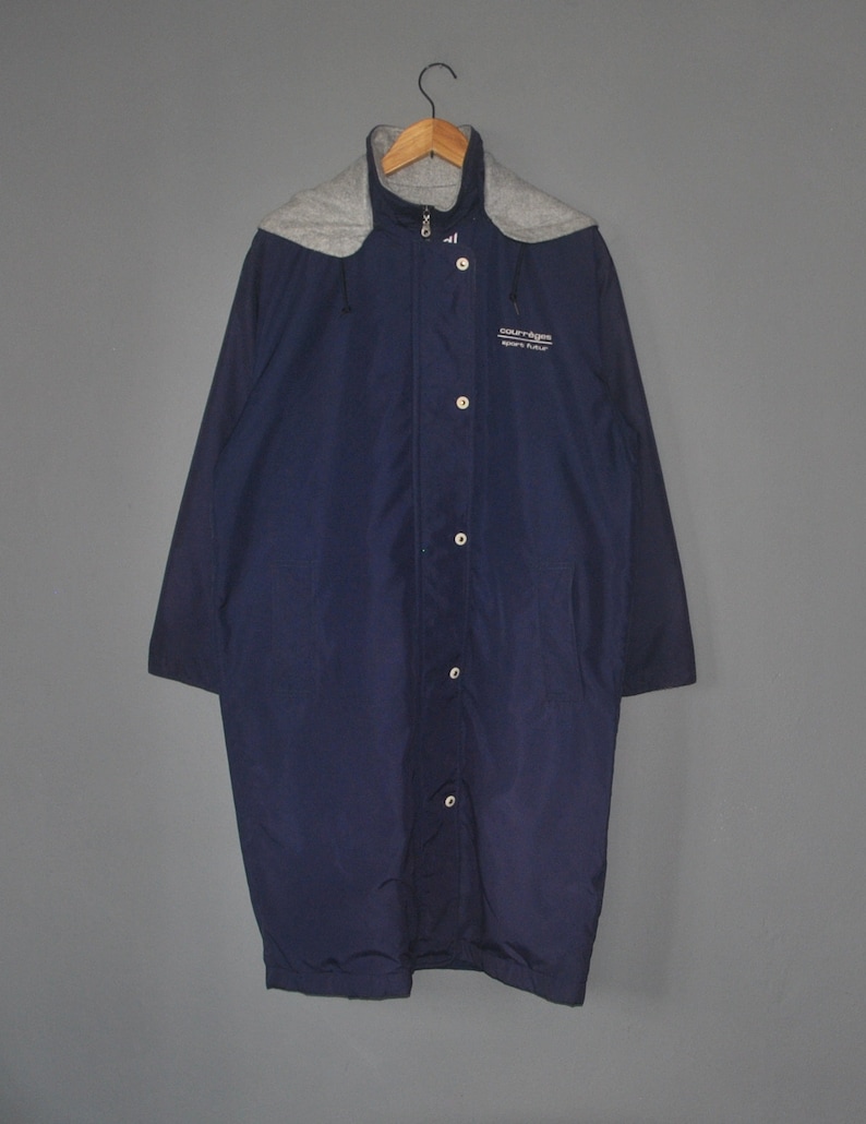 Puede incluir: Una chaqueta larga de color azul marino con un cuello de capucha gris y cierre de cremallera. La chaqueta tiene una solapa de botones y el texto "Court-A-Fire Sports Field" est&aacute; impreso en la parte delantera.