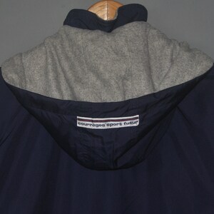 Puede incluir: Una chaqueta azul marino con capucha y forro de polar gris. La chaqueta tiene una etiqueta blanca y roja con el texto "Courreges Sport Futur".