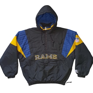 Puede incluir: Chaqueta anorak de los Rams negra, azul y amarilla con capucha. La chaqueta presenta el nombre del equipo en letras doradas en el pecho y el logotipo de la NFL en la manga. La chaqueta tiene un logotipo de Starter en la manga.