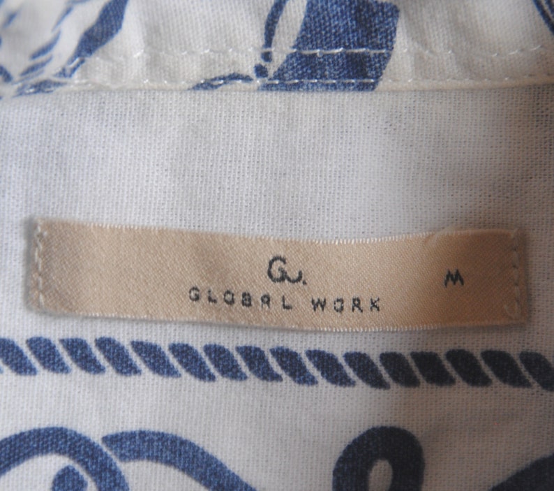 May include: A beige clothing tag with the text "Gu. GLOBAL WORK M" printed in black.