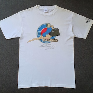 May include: White t-shirt with a graphic of a woman in a blue dress and a black briefcase, with the text "BLUE ANGEL" and "Mesa Boogie Ltd. Petaluma, California". The right sleeve has the text "Recto".