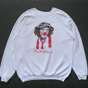 May include: White sweatshirt with a black and white illustration of a clown with a red nose and a red bow tie. The text "Emmett Kelly Jr." is printed below the illustration.