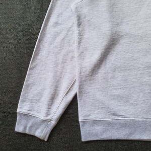 May include: Close-up of a light gray sweatshirt sleeve and hem. The sleeve has a ribbed cuff and is attached to the body of the sweatshirt. The fabric appears to be a soft, knit material.